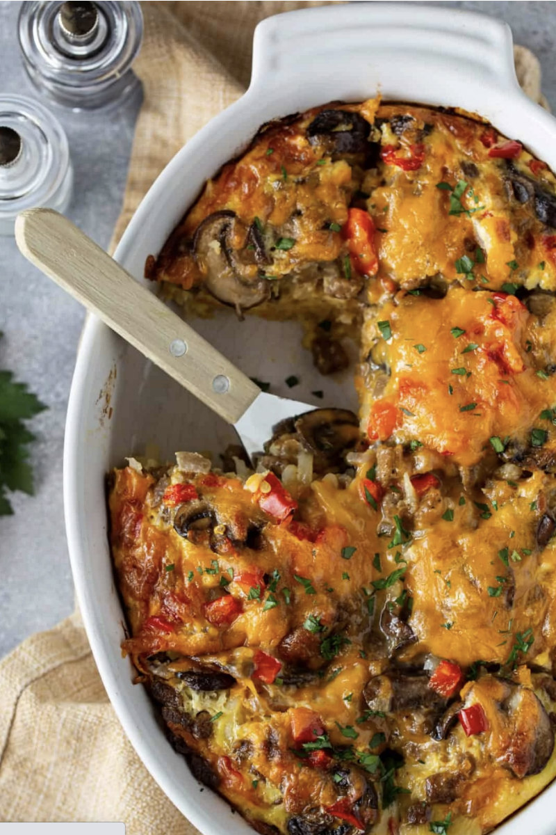 cheesy sausage hash brown egg casserole with spatula in baking dish