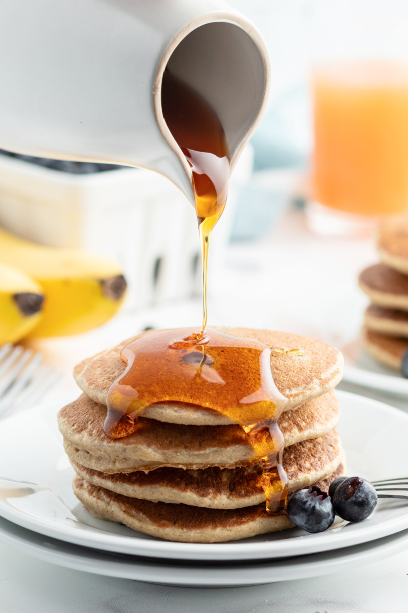 pouring syrup onto a stack of pancakes