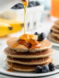 pouring syrup onto stack of blueberry pancakes