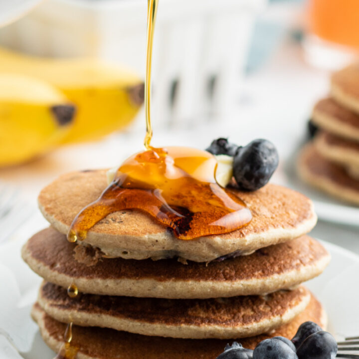 pouring syrup onto stack of blueberry pancakes