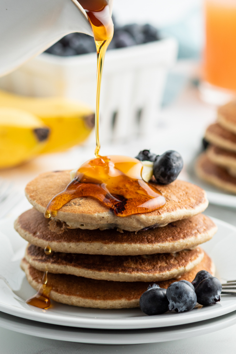 pouring syrup onto stack of blueberry pancakes
