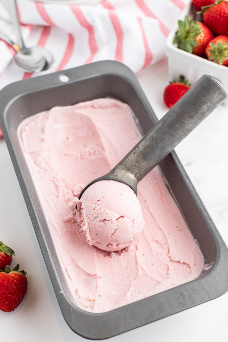 scooping strawberry ice cream out of a container