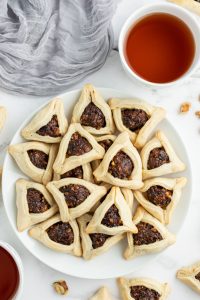 white plate of hamantaschen cookies piled on top