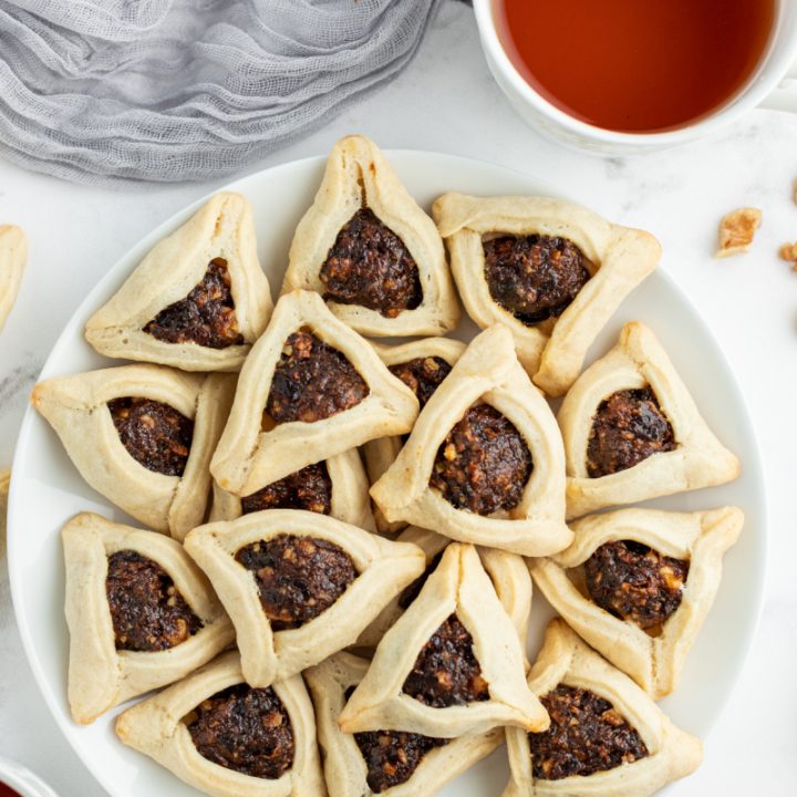 white plate of hamantaschen cookies piled on top