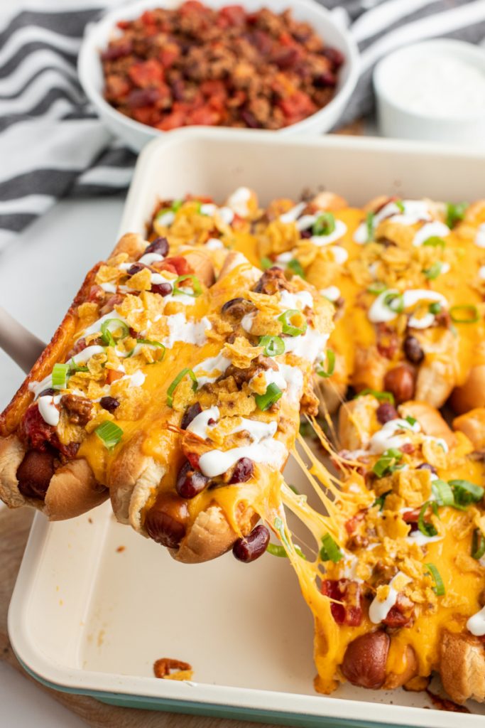 spatula pulling two chili dogs out of casserole dish