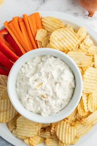 caramelized onion dip in bowl surrounded by chips and veggies