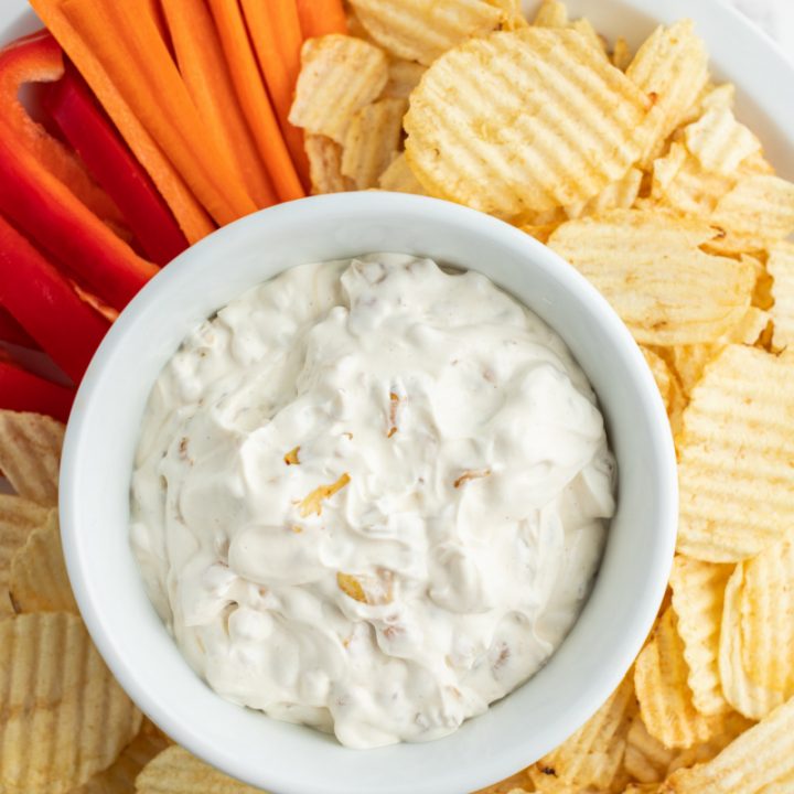 caramelized onion dip in bowl surrounded by chips and veggies