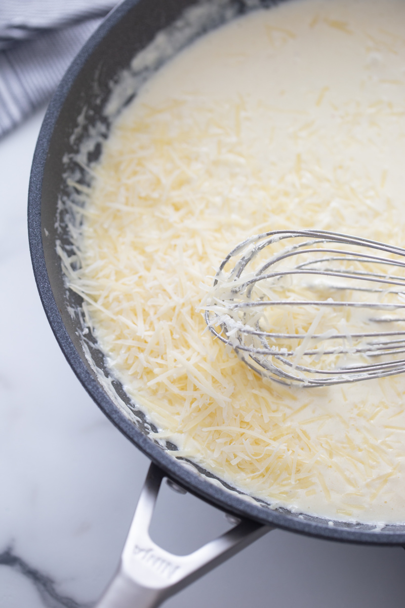 whisking alfredo sauce in skillet