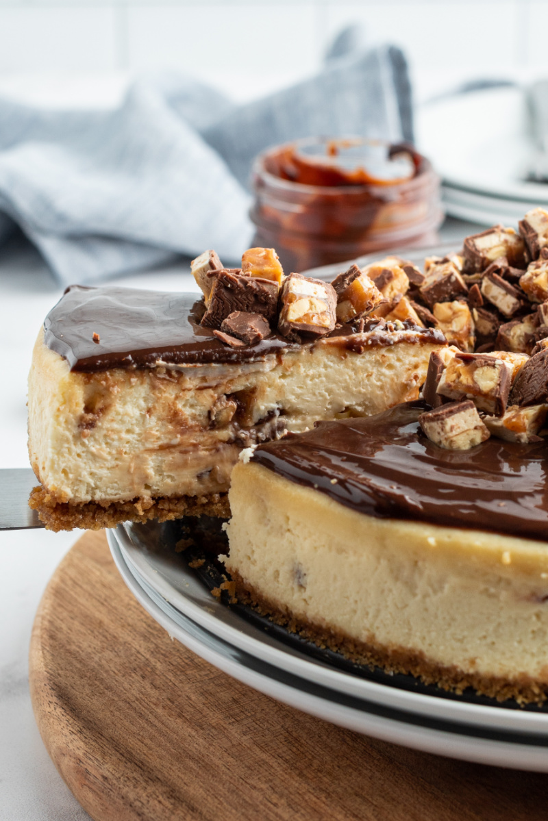 slice of white chocolate snickers cheesecake being removed from the whole cheesecake