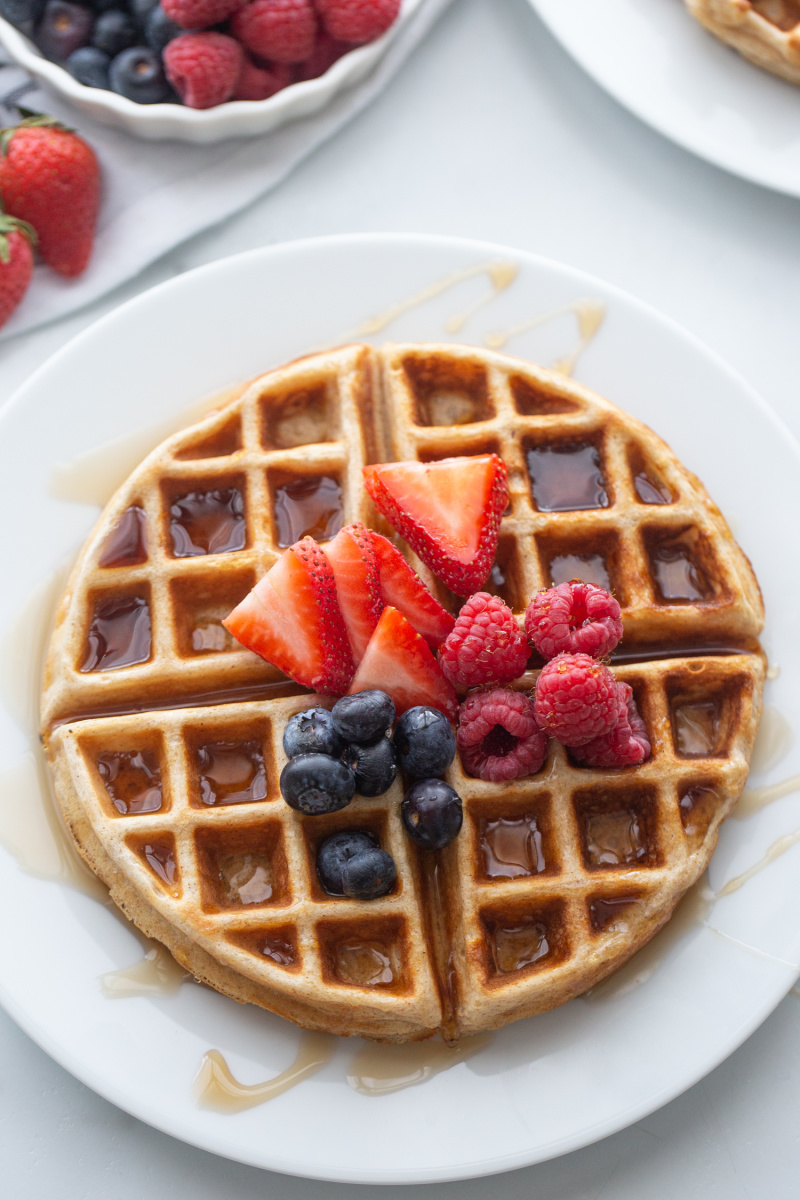 waffle on a white plate topped with syrup and berries