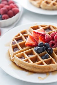 whole grain buttermilk waffle on white plate with syrup and berries