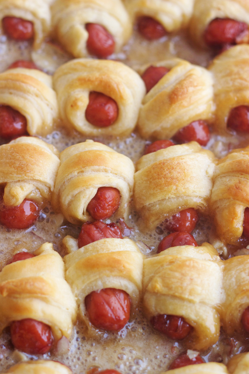 caramelized pigs in a blanket sizzling on a baking sheet