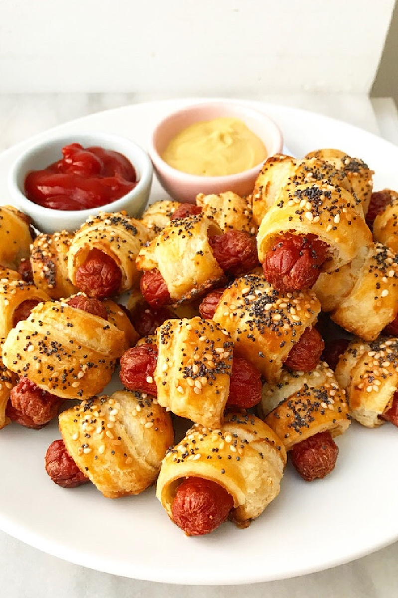 puff pastry pigs in blanket on a white platter with ketchup and mustard
