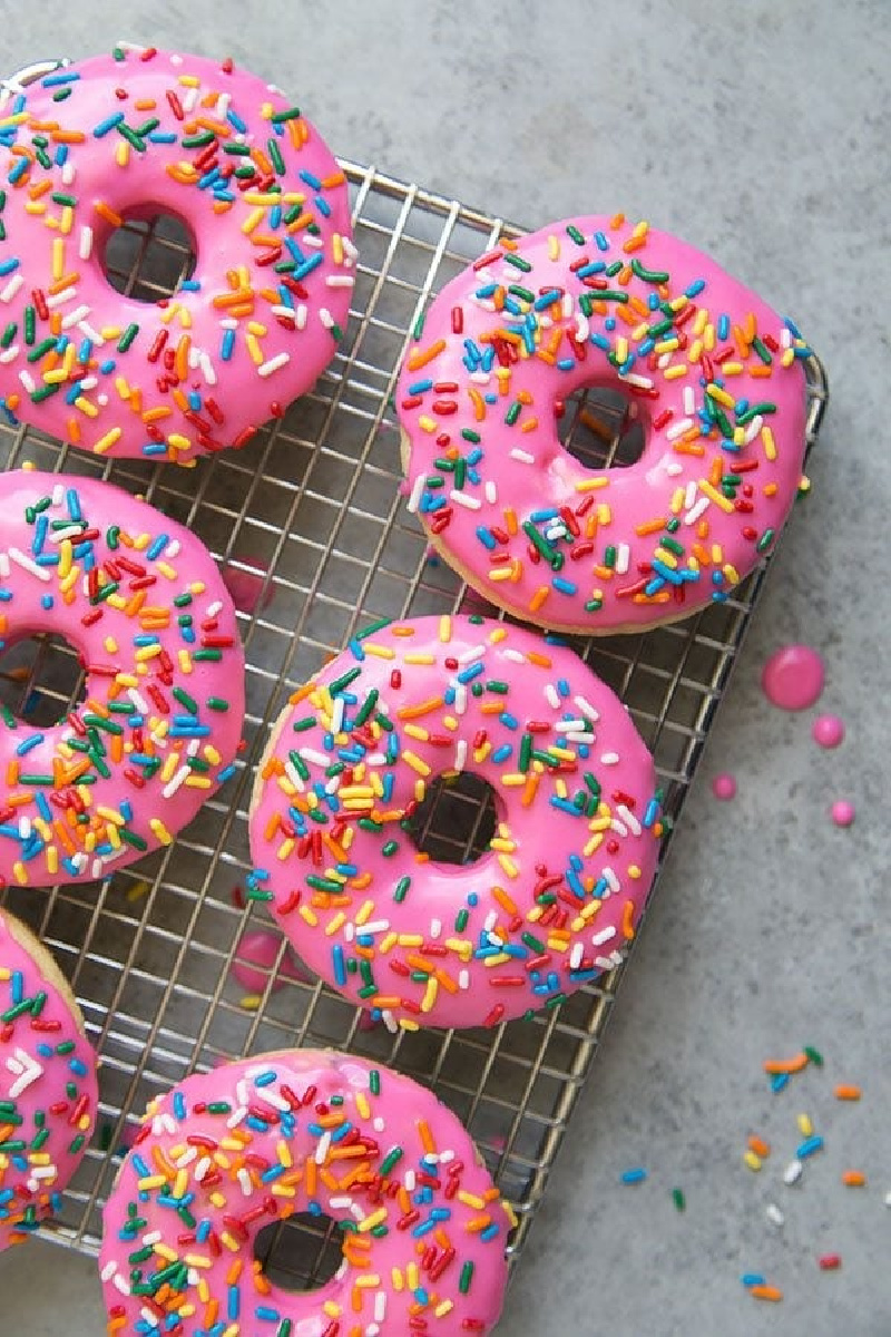 birthday cake doughnuts with pink glaze and sprinkles on cooling rack