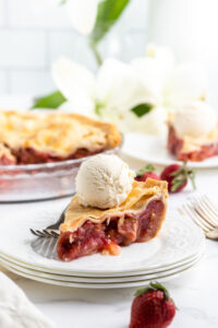 slice of strawberry rhubarb pie on a white plate topped with vanilla ice cream