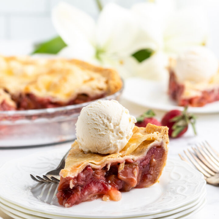slice of strawberry rhubarb pie on a white plate topped with vanilla ice cream
