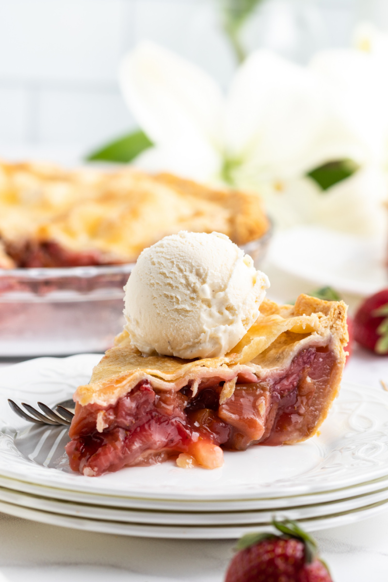 slice of strawberry rhubarb pie on a white plate topped with vanilla ice cream