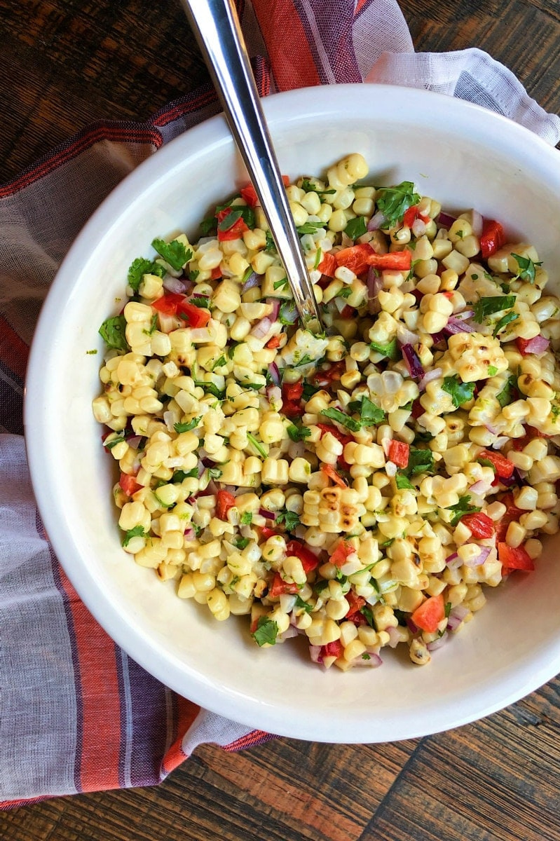 grilled corn salad in white bowl with serving spoon