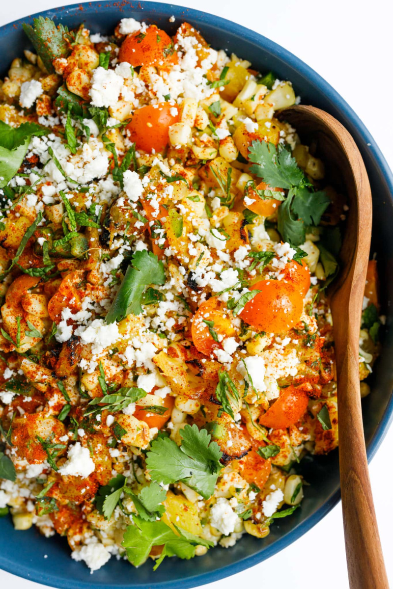 grilled corn and pineapple salad in black bowl with serving spoon