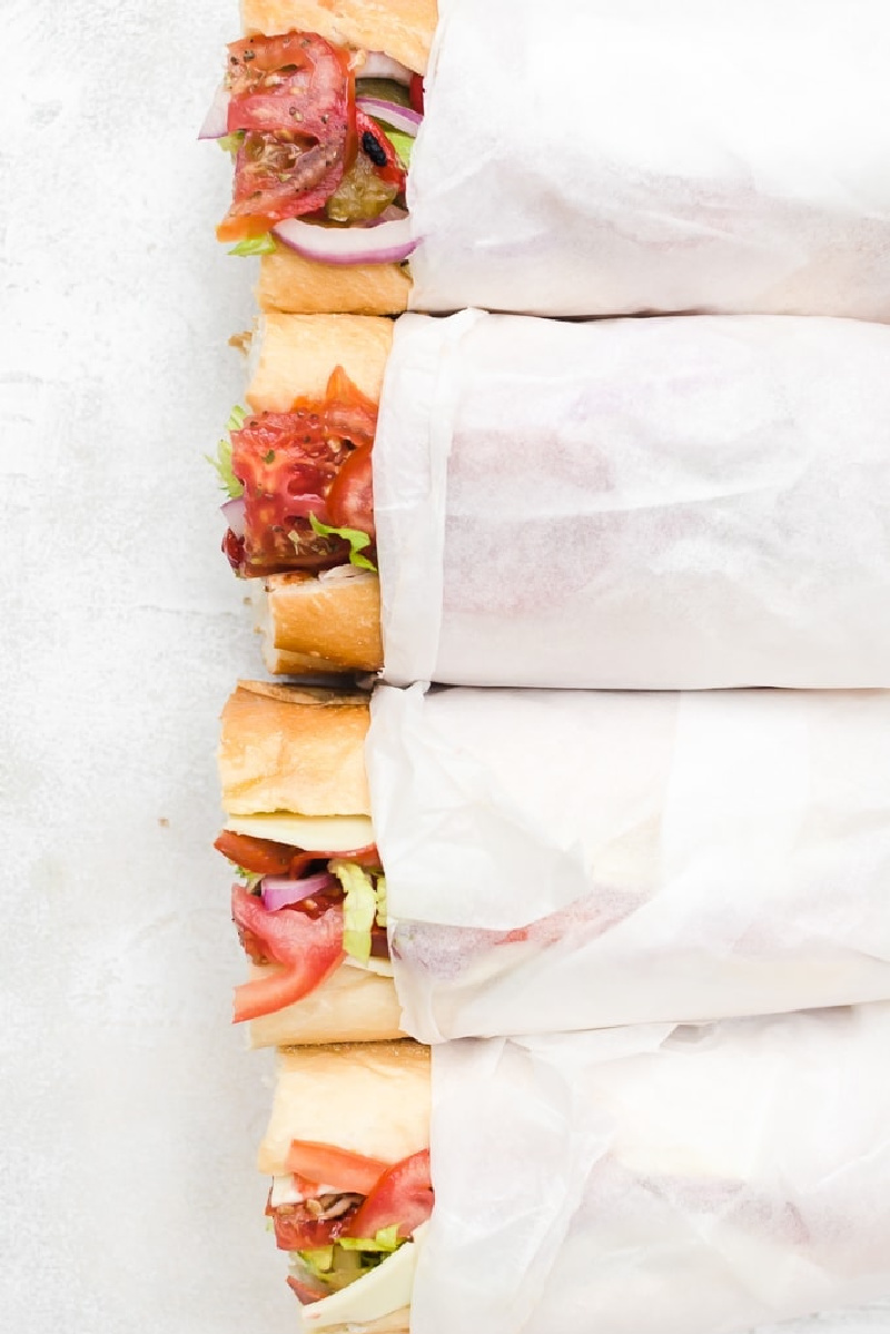 wrapped hoagies with a peek at the end of the sandwiches sticking out of the wrap