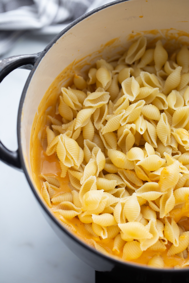 adding pasta to cheese sauce to make mac and cheese