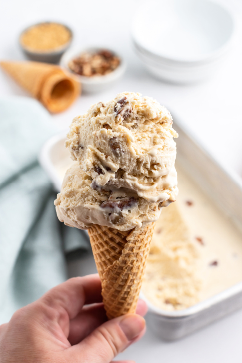 hand holding ice cream cone with scoops of butter pecan ice cream