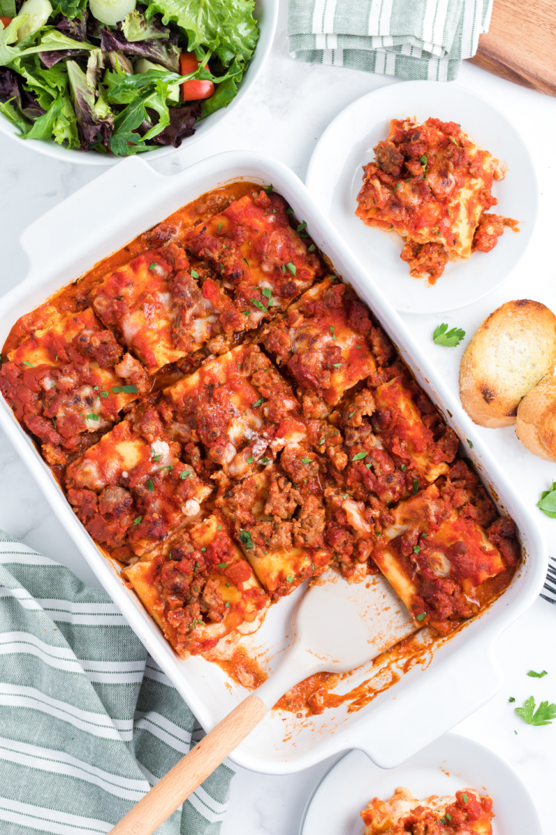 italian sausage lasagna rolls ups in a casserole dish with a couple taken out