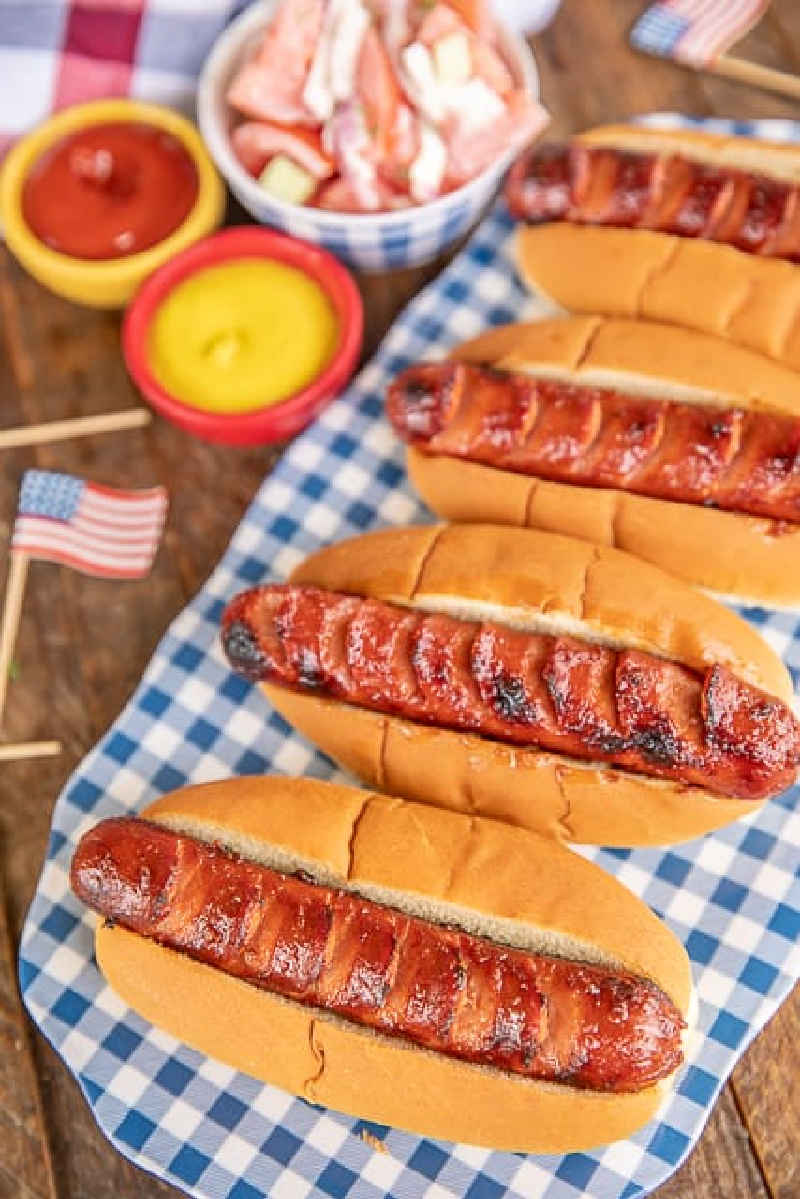 row of marinated grilled hot dogs on a blue and white checked platter