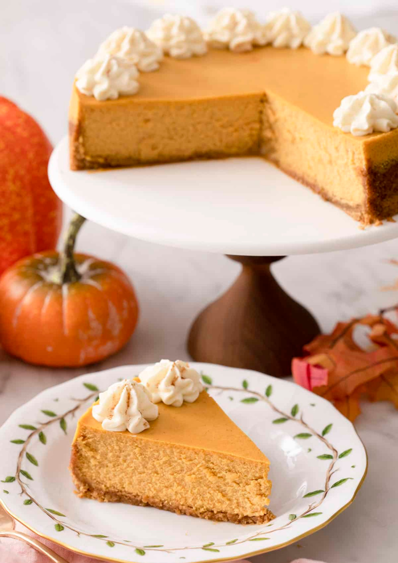 slice of pumpkin cheesecake on a plate with the rest of the cheesecake in background