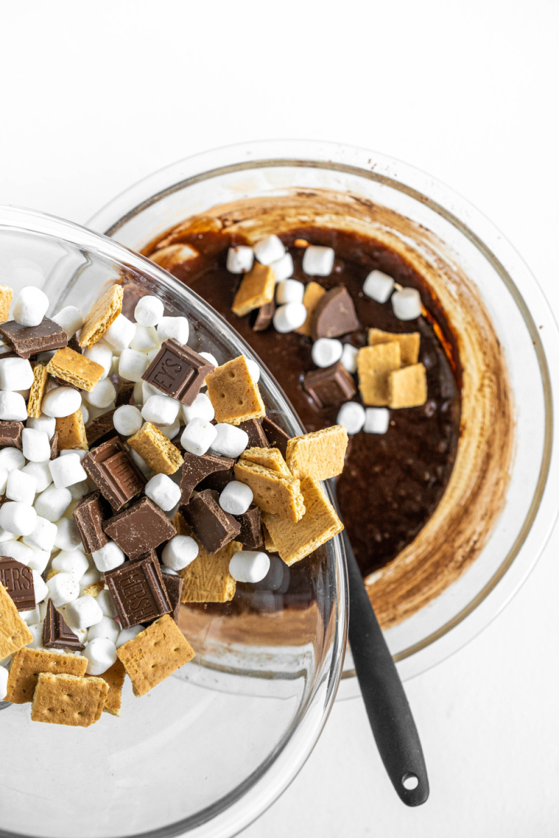 pouring s'mores ingredients into brownie batter in bowl