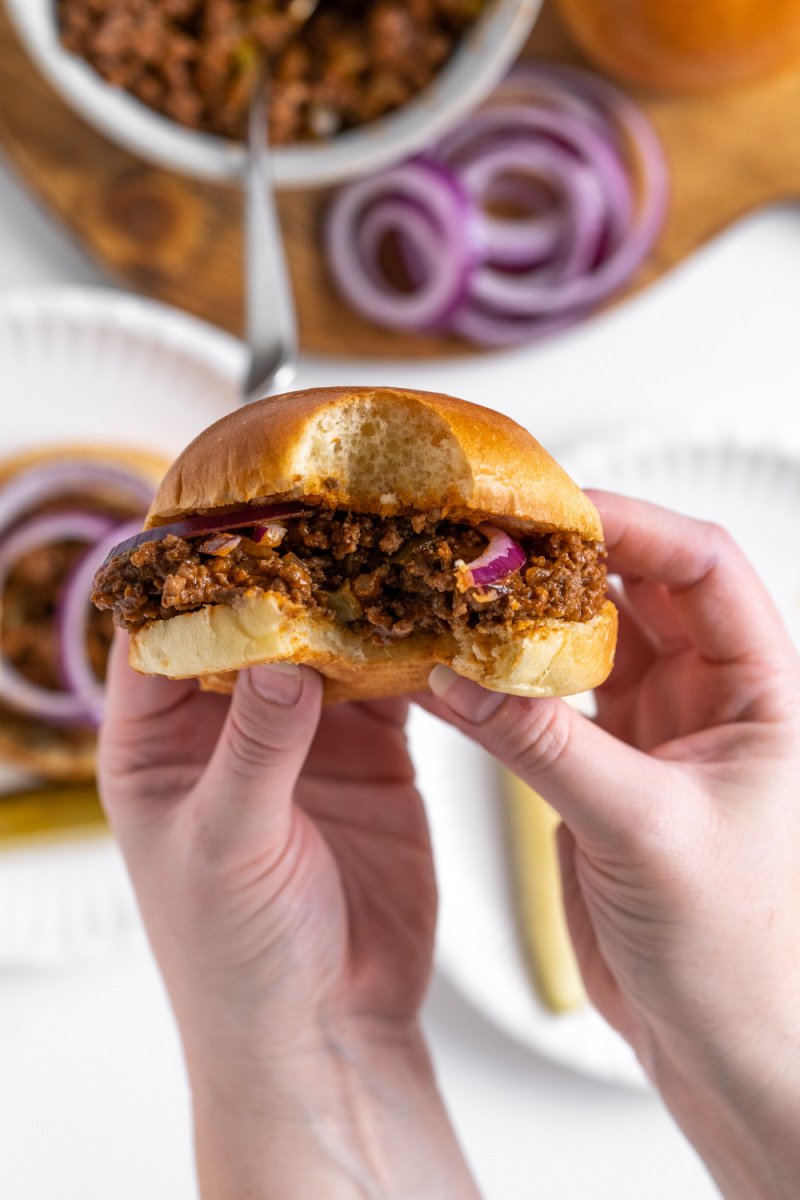 hands holding sloppy joe with bite taken out of it