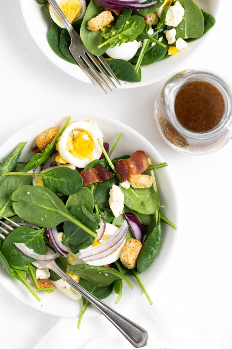 plate of spinach salad with dressing on side