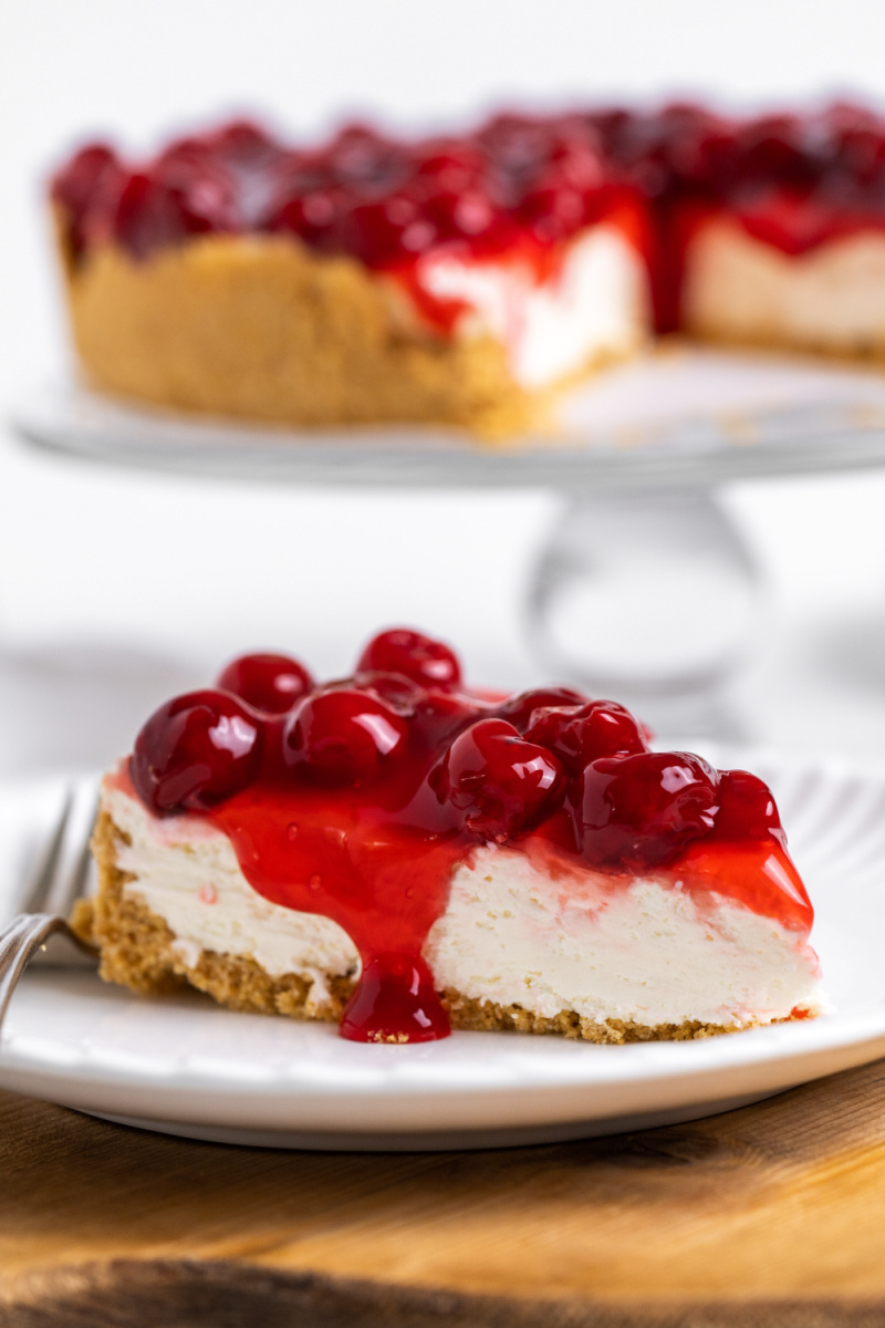slice of cherry cheesecake on plate with rest of cheesecake in background