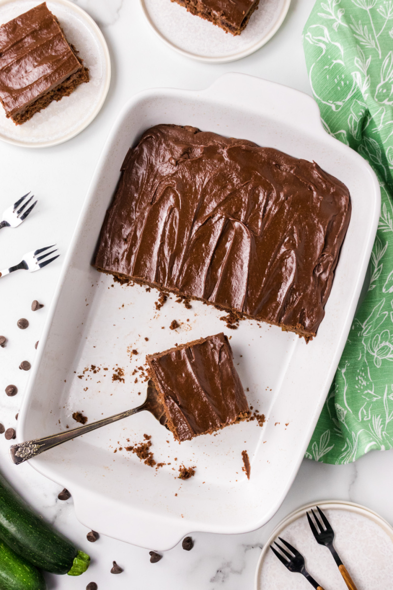 chocolate zucchini cake in a baking dish with spatula taking out slice