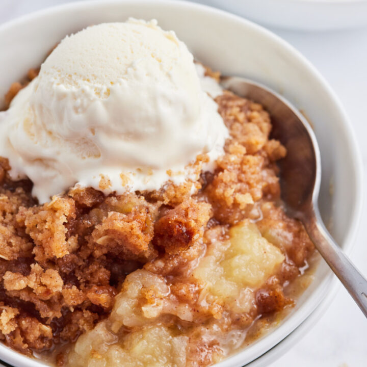 apple betty in a bowl topped with vanilla ice cream