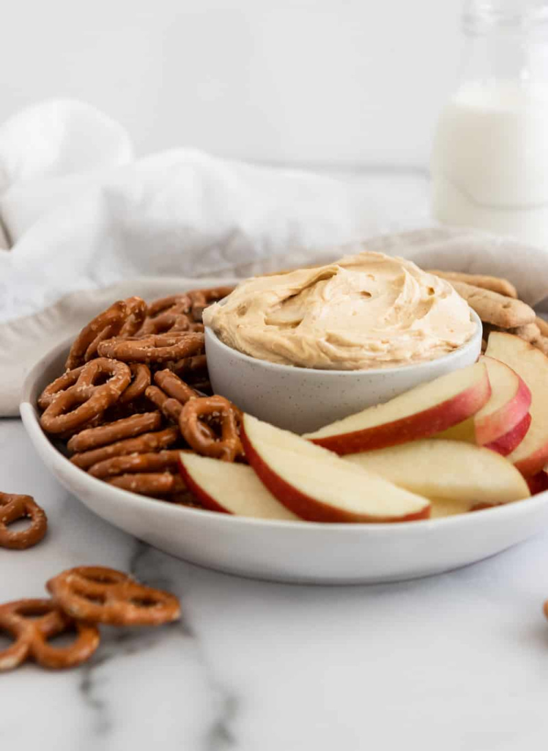peanut butter greek yogurt dip in a dish with pretzels and apples