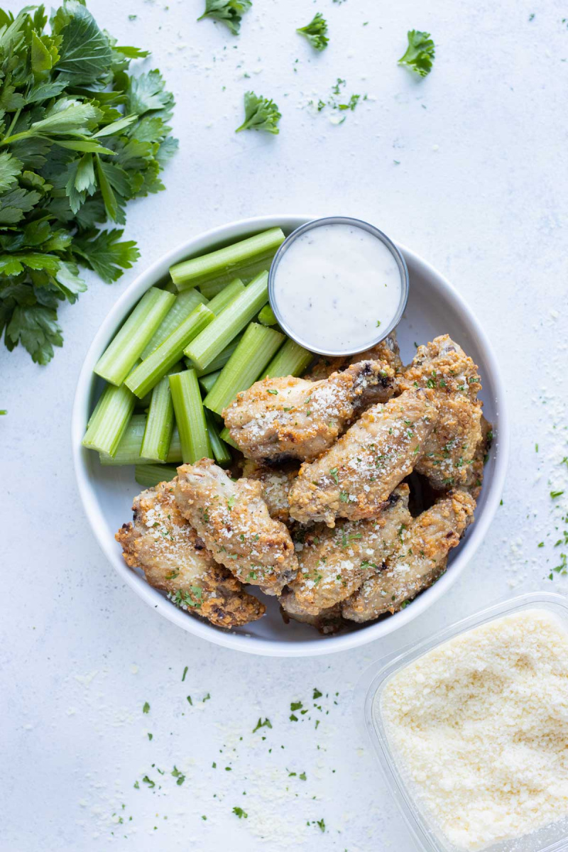 bowl of parmesan garlic baked chicken wings with celery and sauce
