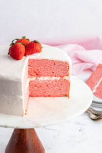 strawberry cake on stand with big slice taken out of it