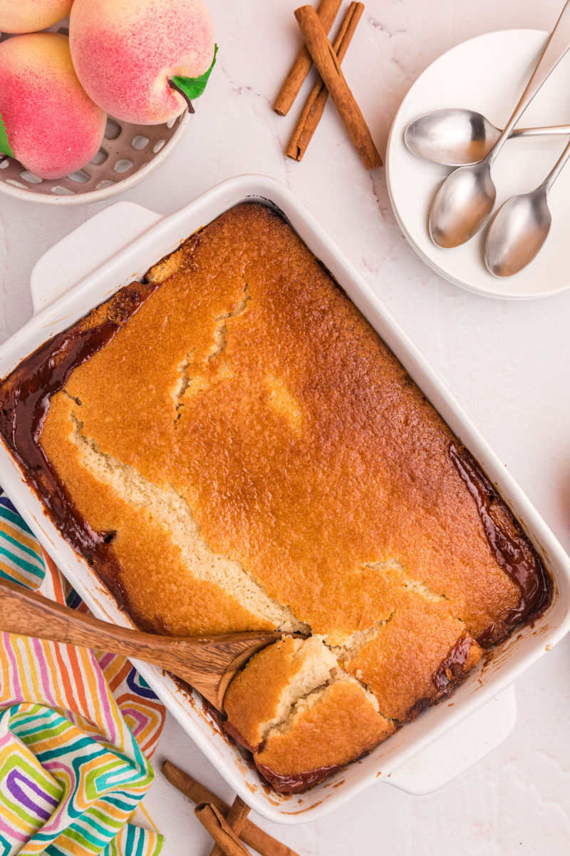 peach cobbler in pan with wooden spoon in it