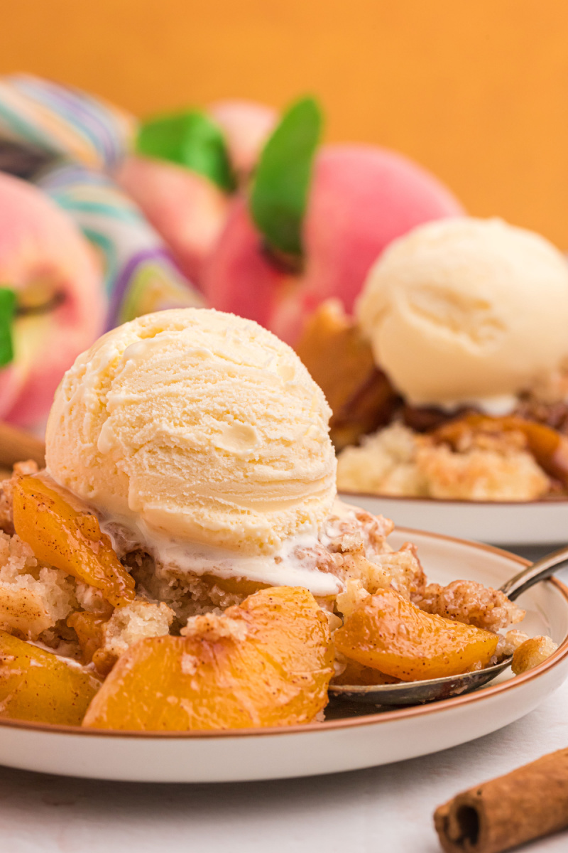 serving of peach cobbler on plate with scoop of vanilla ice cream on top