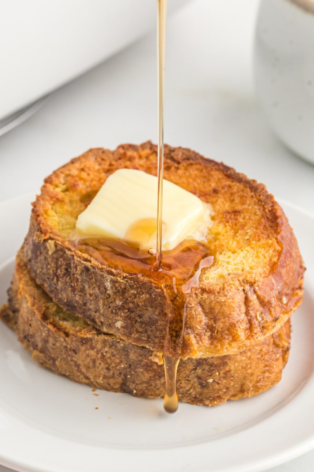 two slices baked french toast with pat of butter and syrup