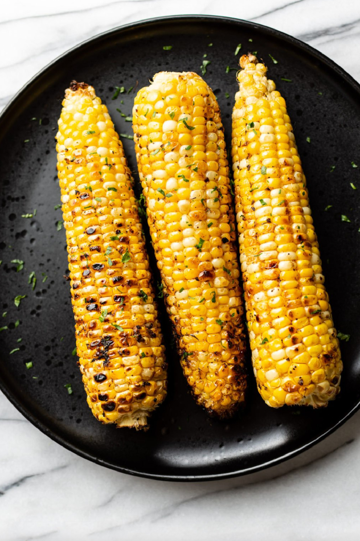 three cajun grilled corn on the cob on black plate