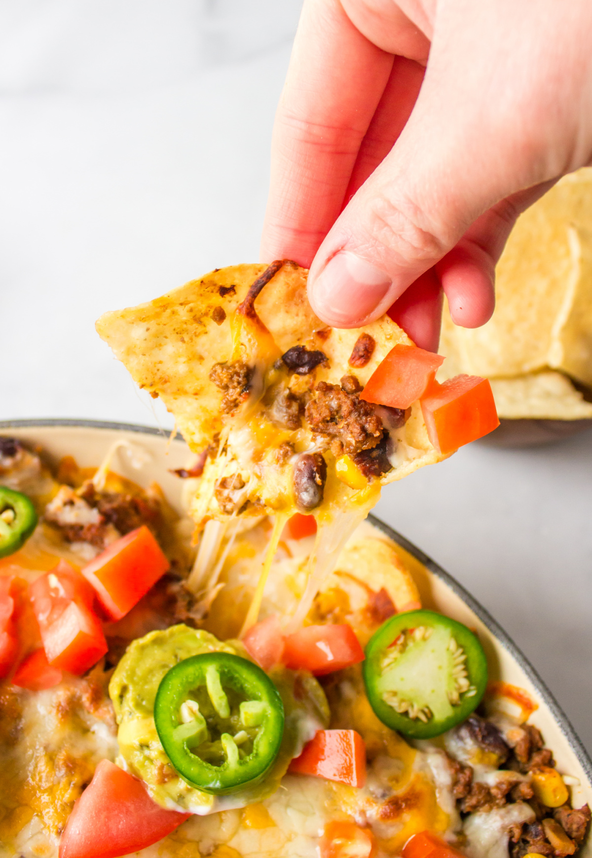 hand pulling cheese pulled nacho out of pan