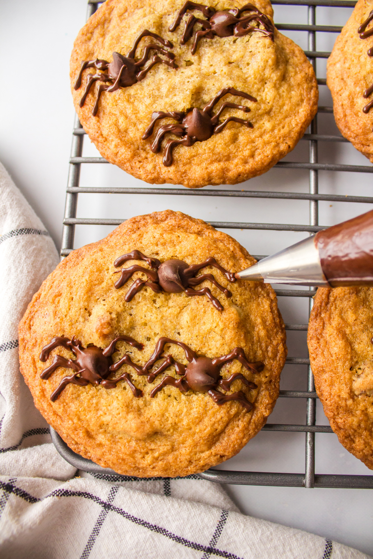 piping chocolate spiders onto chocolate chip cookies