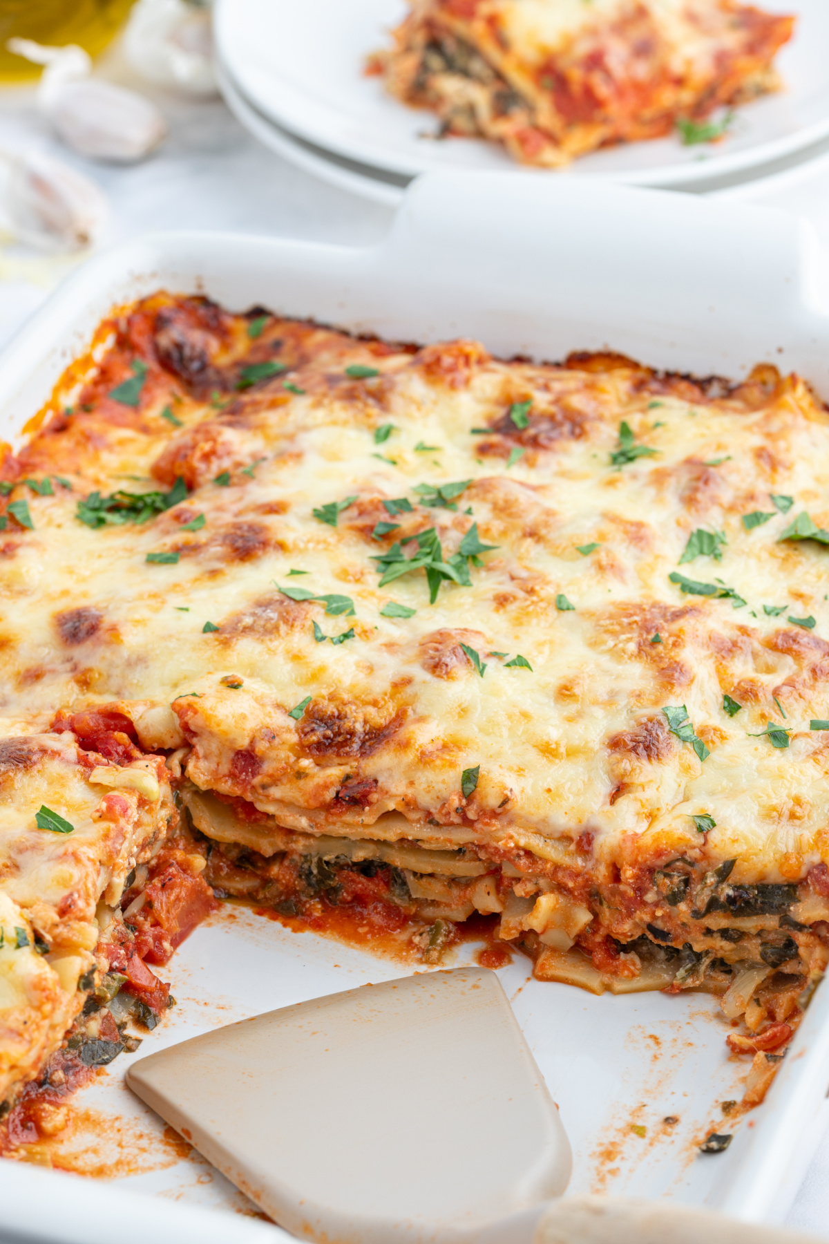 spinach artichoke lasagna in baking dish with slices taken out of it